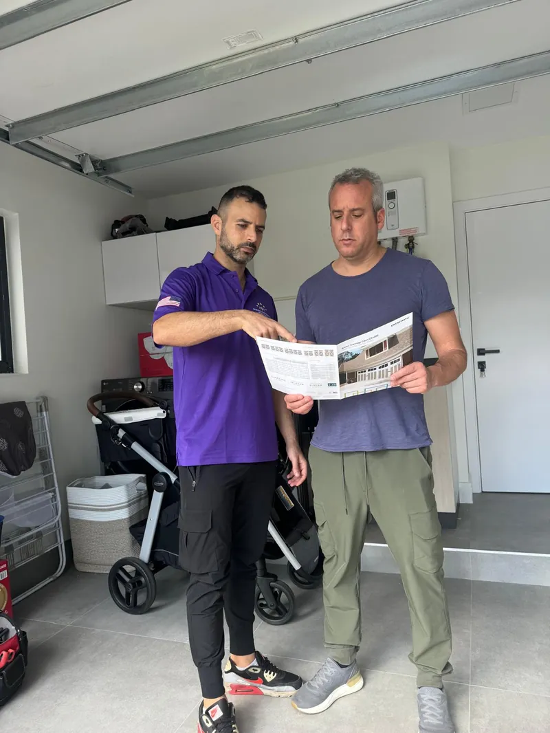 Garage Door Kingdom technician in branded purple uniform explaining new garage door options from a manufacturer brochure to a Broward County homeowner