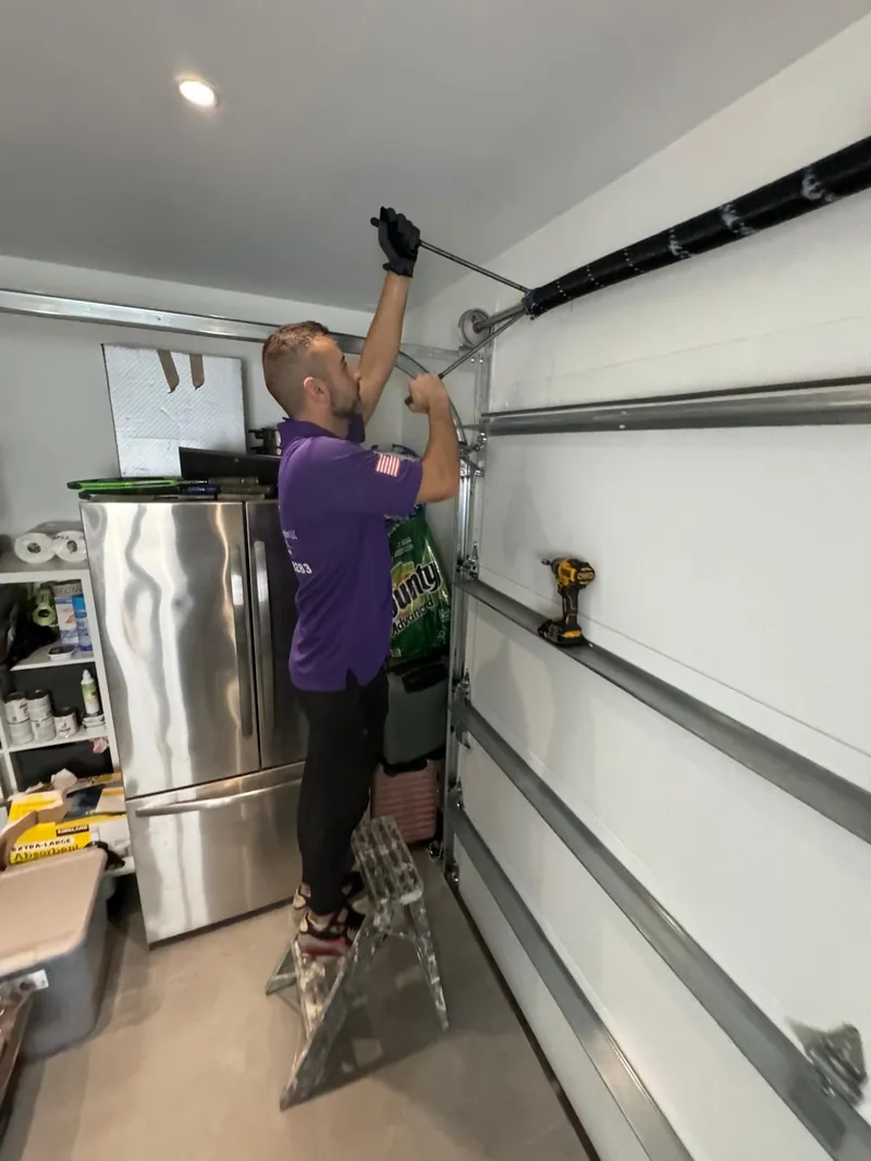 Garage Door Kingdom licensed technician wearing gloves and uniform replacing a torsion spring on a residential garage door in Broward County, FL